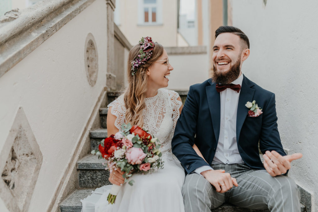 Lachendes Brautpaar sitzt vor dem Standesamt auf einer Treppe | Portraitbilder in der Natur | Hochzeitsreportage im Landkreis Fürstenfeldbruck Ammersee Landsberg München
