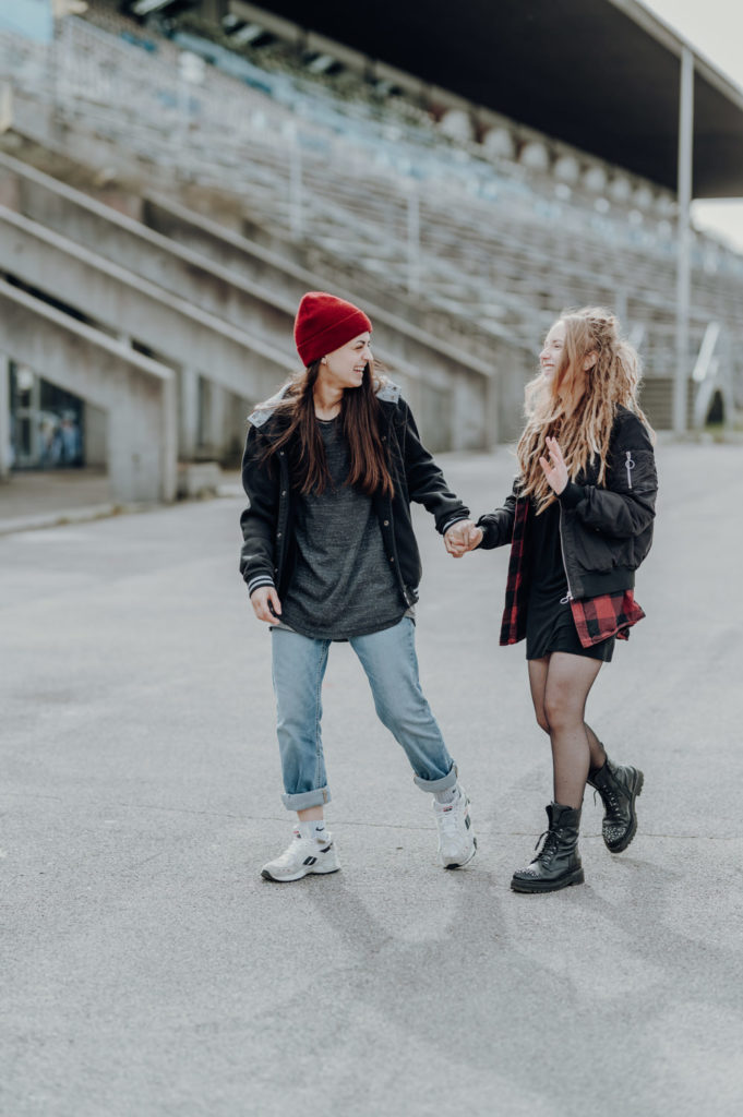 Pärchenshooting an der Ruderregatta in München. Lesbisches Paar läuft händchenhaltend | Fotografin in der Region München Ammersee Fürstenfeldbruck