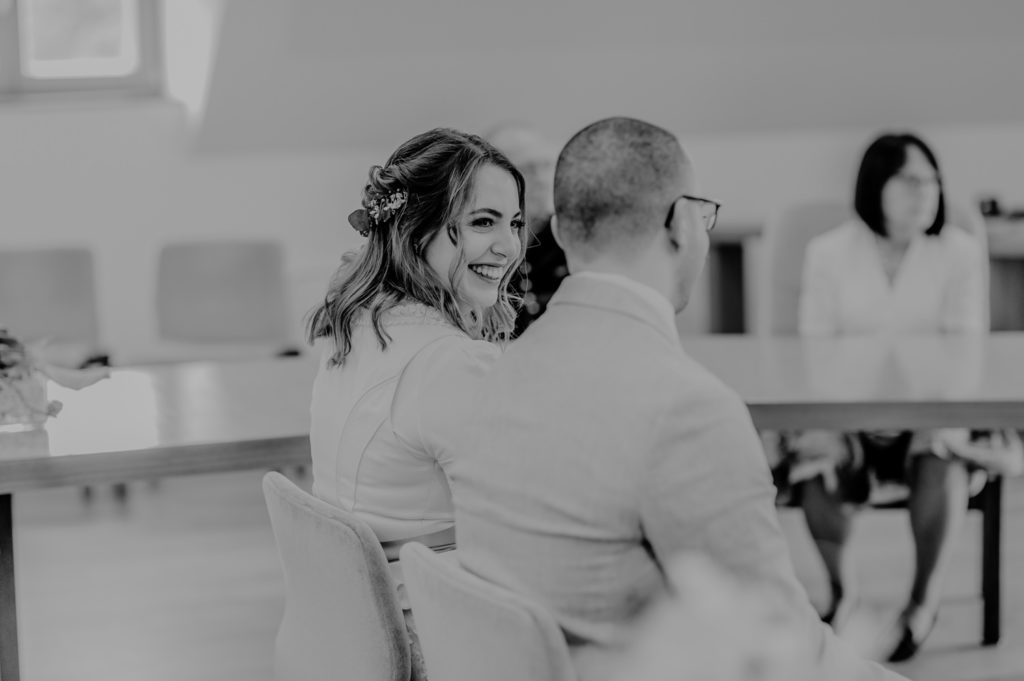 Schwarzweißaufnahme Braut lächelt Bräutigam im Trausaal an | Fotografin in Landsberg am Ammersee Fürstenfeldbruck München