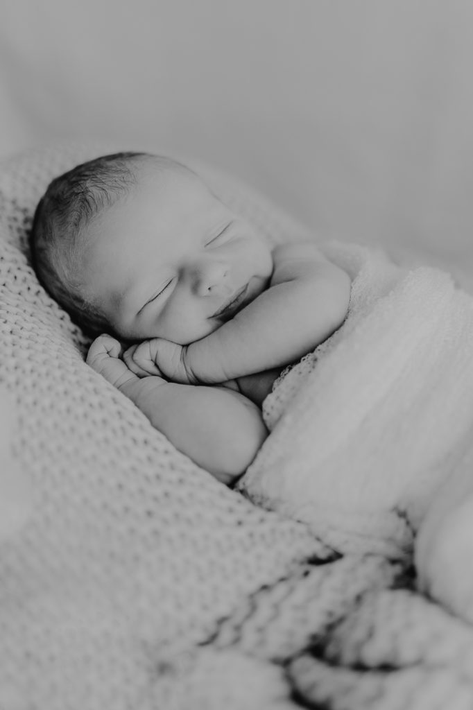Newbornfotografie. Kind liegt in einem mit Fell ausgelegten Körbchen und schläft.