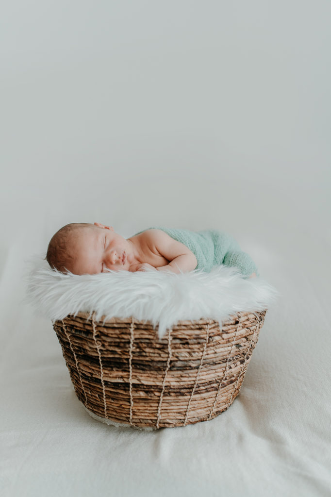 Newbornfotografie. Kind liegt in einem mit Fell ausgelegten Körbchen und schläft.